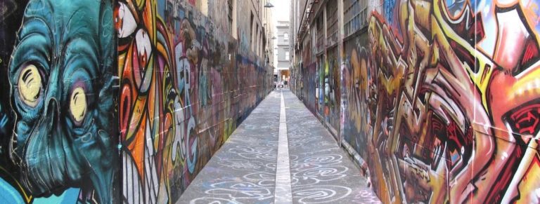Image of Union Lane, a small city lane full of art. Up close on the left is a blue skull and on the right wall is red graphic writing.